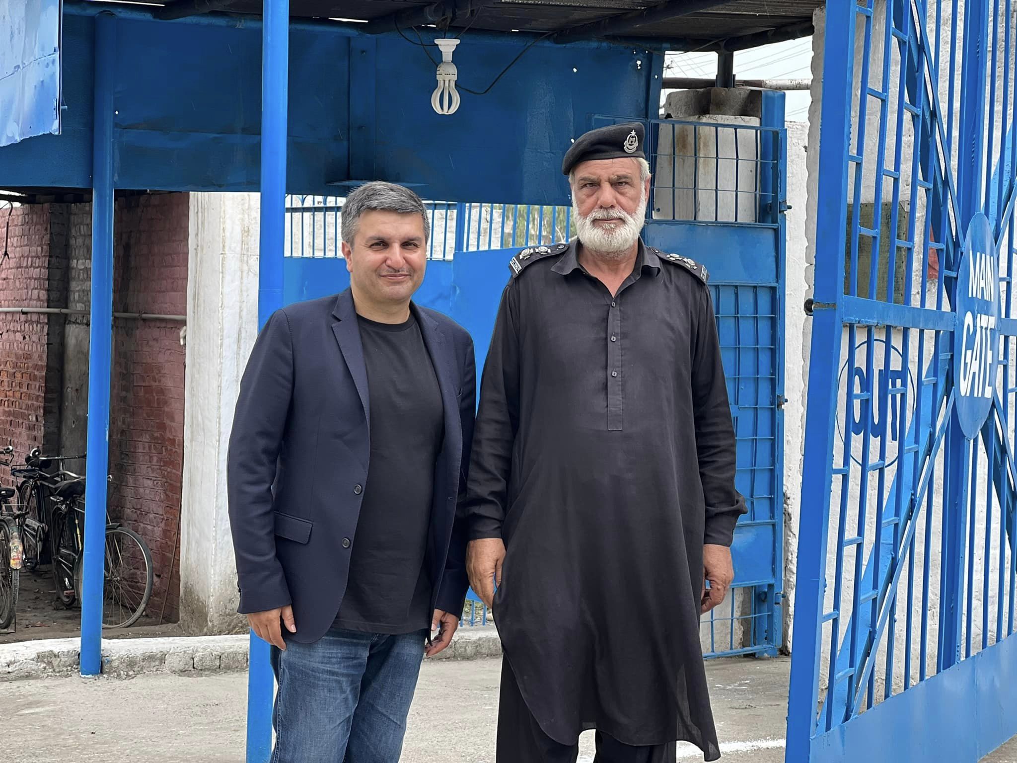 Two men standing at a security gate, one in a police uniform and the other in a blazer